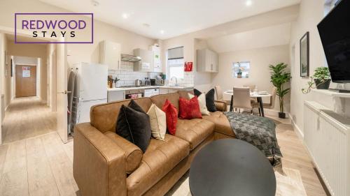 a living room with a brown couch and a kitchen at Newly Refurbished Everest Lodge Serviced Apartments for Contractors & Families, FREE WiFi & Netflix by REDWOOD STAYS in Farnborough
