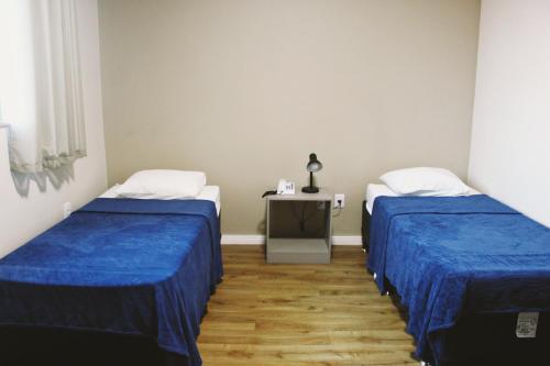 two beds in a room with blue sheets and a table at Hotel Pousada Del Rey in Macaé