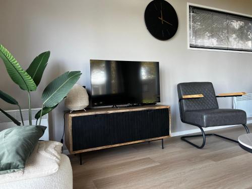 a living room with a tv and a chair and a clock at Boshuisje 15 in Haarle