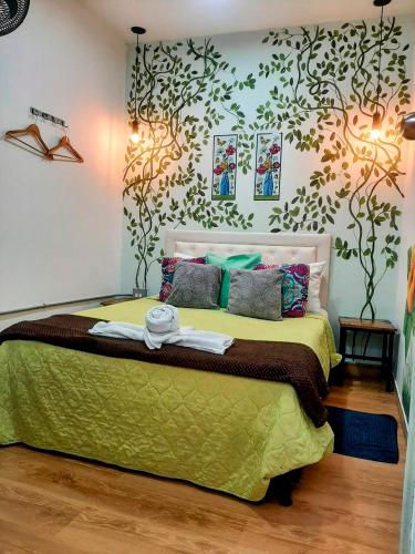 a bedroom with a bed with green sheets and trees on the wall at Hotel Boutique Stay La 10 in Medellín