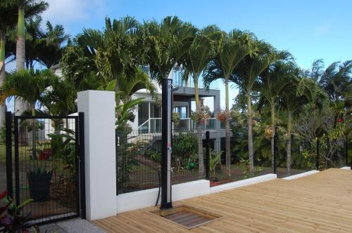 a house with palm trees behind a fence at Grande Villa au calme - Vue exceptionnelle - Climatisation - Piscine sel chauffée - Jardin Tropical in Vincendo