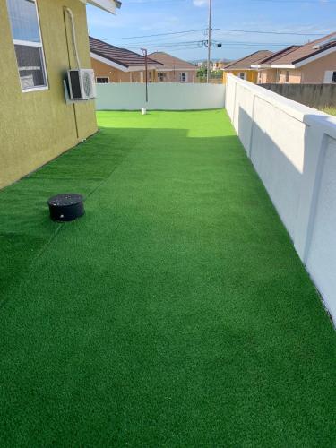 a patio with green grass and a black tire on it at Harbour Oasis Retreat - Charming 2 Bedroom House in Old Harbour