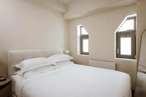 a bedroom with a white bed with two windows at Likno Athens in Athens
