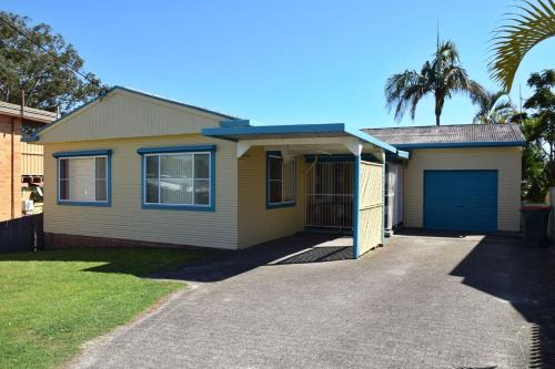 a yellow house with a garage and a palm tree at Seamist Cottage - Bring your own linen. in South West Rocks