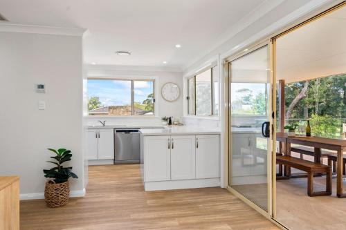 a kitchen with white cabinets and a dining room with a table at Beaches n Birdies in Mollymook