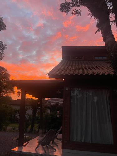 a sunset behind a house with a table and a chair at CHALÉ DOS ALPES VERDES in Canela