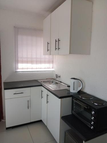 a kitchen with white cabinets and a sink and a microwave at Baksman's Retreat in Soweto