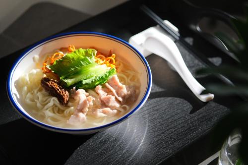 a bowl of noodles with meat and vegetables on a table at Lane Wisdom Garden Hotel - Lijiang Ancient City Zhongyi Market in Lijiang