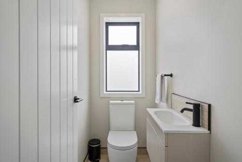 a white bathroom with a toilet and a sink at Wharewaka Escape - Taupo in Taupo