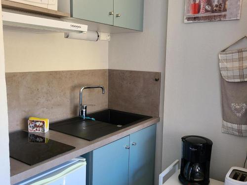 Elle comprend une petite cuisine avec un évier et des placards bleus. dans l'établissement Studio cabine au pied des pistes – 4 pers, balcon - FR-1-689-150, à Villard-de-Lans