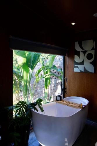 una bañera blanca frente a una ventana con una planta en Đòng Đòng Lodge, en Ấp Ðông Ðô