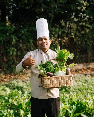a man wearing a chef hat holding a basket of vegetables at Kasara Chitwan in Chitwan