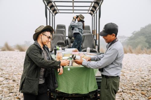 a man handing another man a plate of food at a table at Kasara Chitwan in Chitwan
