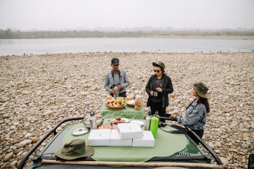 a group of three people standing around a table on a beach at Kasara Chitwan in Chitwan