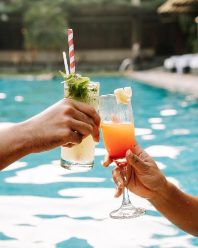 two people holding drinks next to a swimming pool at Kasara Chitwan in Chitwan