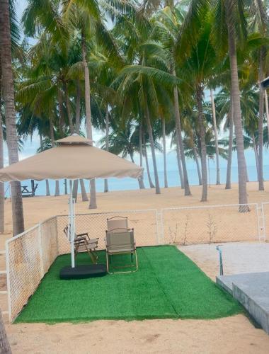 a beach with a chair and an umbrella on a patch of grass at W Sichon Beachfront Homestay in Ban Kho Khao