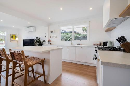 a kitchen with white cabinets and a counter and chairs at Hamptons on Heales - Classic Beach House Charm in Dromana