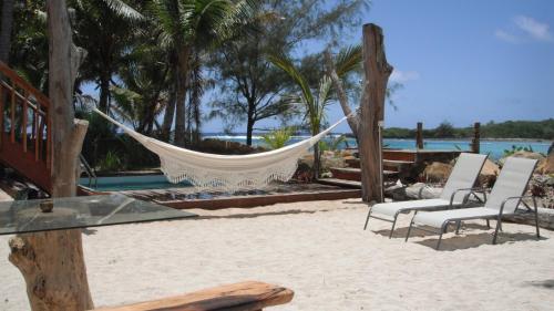 a hammock on a beach with chairs and the water at Kaireva Beach House in Rarotonga