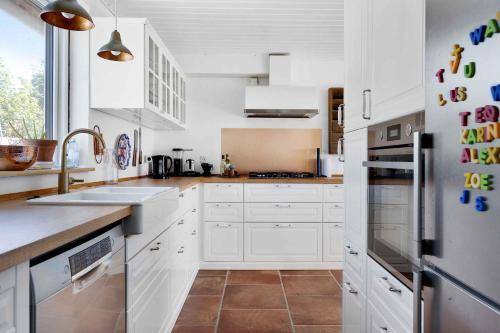 a kitchen with white cabinets and a stainless steel refrigerator at Summerhouse With Both Island Charm And Sea View in Holbæk