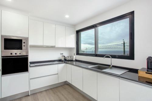 a kitchen with white cabinets and a large window at Villa Angela in Funchal