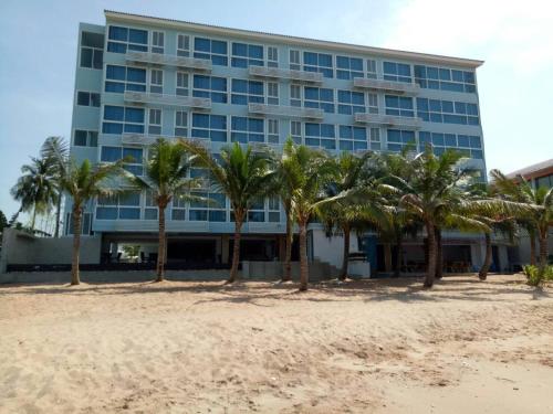 a building on the beach with palm trees in front at Nantra Pattaya Baan Ampoe Beach in Na Jomtien