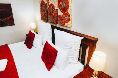 a bedroom with a white bed with red pillows at Ehrlichpark Lodge self catering and spa in Bloemfontein