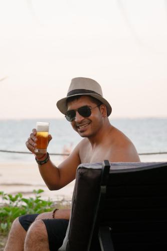 a man sitting in a chair holding a glass of beer at LalaGalu - Beachfront EcoCabins in Diani Beach