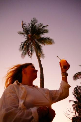 a woman standing next to a palm tree holding a drink at LalaGalu - Beachfront EcoCabins in Diani Beach