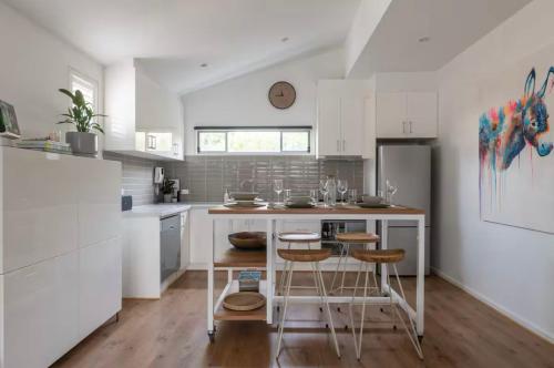 a kitchen with white cabinets and a table and stools at Designer townhome adjacent to East Brunswick Village 2min to tram plus private parking in Melbourne