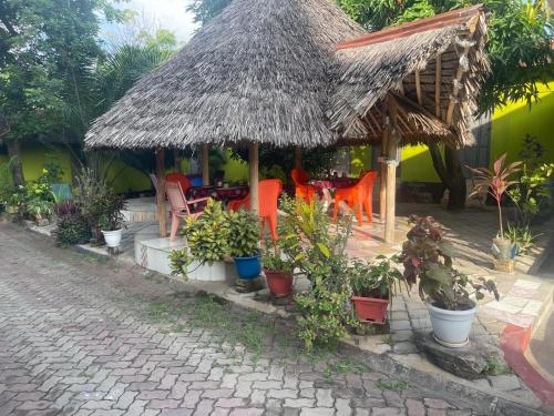 a restaurant with a straw roof and chairs and plants at L&J Modern Backpackers Kinondoni in Dar es Salaam
