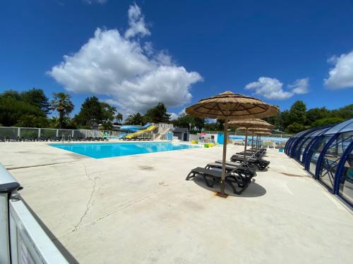 - un groupe de chaises et un parasol à côté de la piscine dans l'établissement Charmant chalet situé dans un camping 4 étoiles - 4 à 6 personnes - TILIO, à Guidel