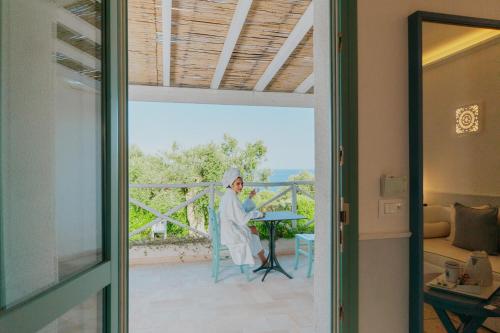 a woman in a robe sitting at a table on a balcony at Marenea Suite Hotel - CDSHotels in Marittima