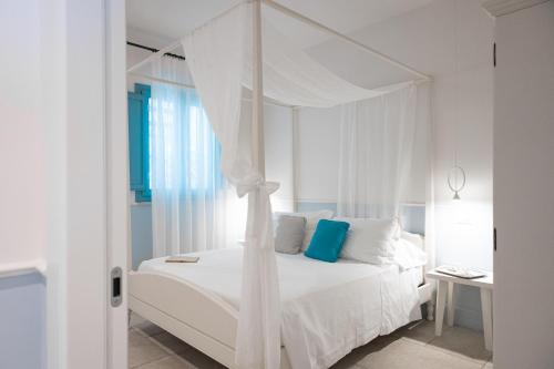a white bedroom with a white canopy bed with blue pillows at Marenea Suite Hotel - CDSHotels in Marittima