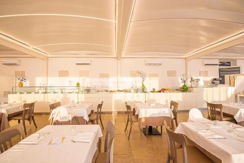 a restaurant with white tables and chairs and a kitchen at Relais Masseria Le Cesine - CDSHotels in Vernole