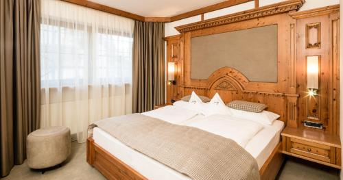 a bedroom with a large bed with a wooden headboard at Savoy Dolomites Luxury & Spa Hotel in Selva di Val Gardena