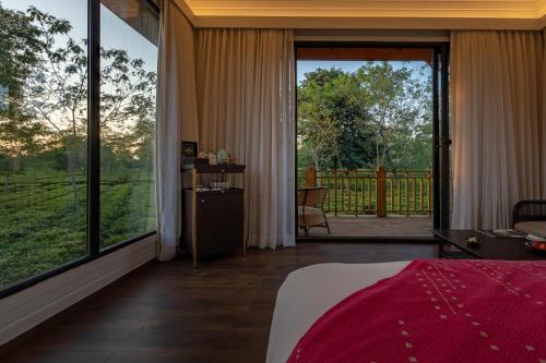 a bedroom with a large window with a view of a yard at The Postcard in the Durrung Tea Estate, Assam in Tezpur