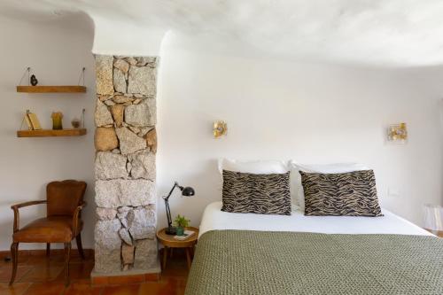 - une chambre avec un lit, une chaise et un mur en pierre dans l'établissement Les Villas de Palombaggia, à Porto-Vecchio