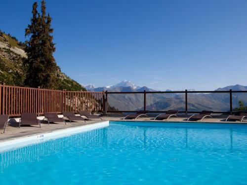 a swimming pool with chairs and mountains in the background at Résidence & Spa Les Sources de Marie - Arc 1950 Le Village in Arc 1950