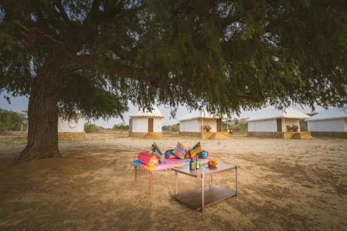 a table under a tree in front of some huts at Desert Vista Camp Jaisalmer in Jaisalmer