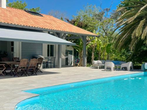 a swimming pool with a table and chairs next to a house at Maison de Famille entre Biarritz et Hossegor in Saint-Martin-de-Seignanx