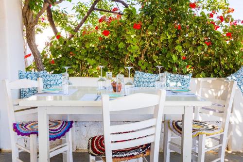 a white table with white chairs and red flowers at Harama Hotel Schinousa in Skhoinoussa