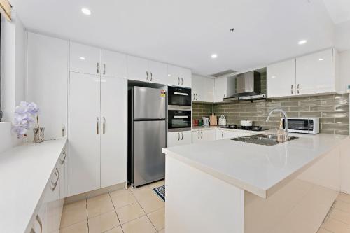 a kitchen with white cabinets and a stainless steel refrigerator at Epic CBD city view 3BR penthouse walk to Station&shopping Centre in Sydney