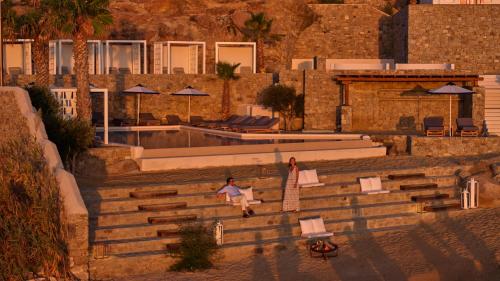 a person sitting on the stairs next to a swimming pool at Mykonos Grand Hotel & Resort in Agios Ioannis Mykonos