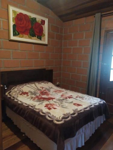 a bed in a room with a painting of roses at Chalé da Lu in Santo Antônio do Pinhal