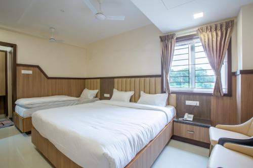 a bedroom with two beds and a chair and a window at Hotel PRM Aruna Archadia in Erode