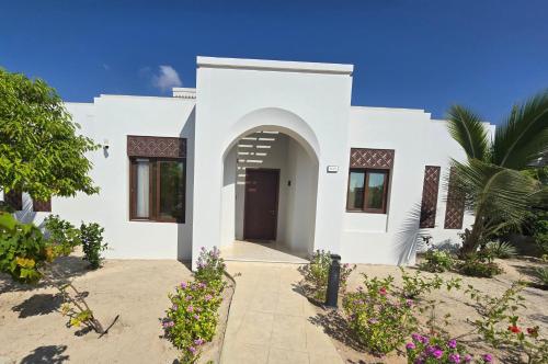 a white house with a door and some flowers at Tulip Star Hawana in Salalah