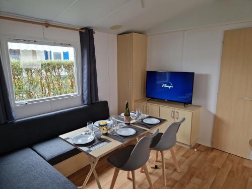 un salon avec une table, des chaises et une télévision dans l'établissement Mobil Home Beg Meil 300m plage avec piscine partagée, terrasse privée et Wi-Fi, à Fouesnant