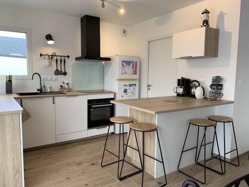 une cuisine avec des armoires blanches et des tabourets de bar dans l'établissement Maison neuve avec jardin, terrasse à PERROS-GUIREC - Réf 918, à Perros-Guirec