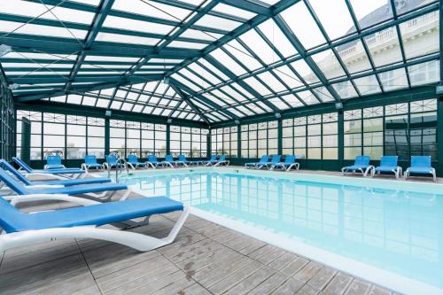 une grande piscine avec des chaises bleues dans un immeuble dans l'établissement Le Studio Goëland, à Trouville-sur-Mer