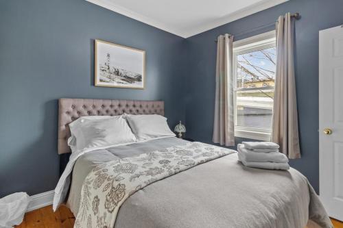 a bedroom with a bed with blue walls and a window at Historic Jelly Bean Row House, Walk To Signal Hill in St. John's